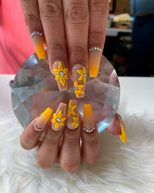 Matte yellow ombre nails with rhinestones on nail base beside 3d sunflowers on two accent nails