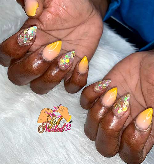 mustard yellow ombre nails short stiletto shaped with two accent clear nails adorned with glitter and gold foil 