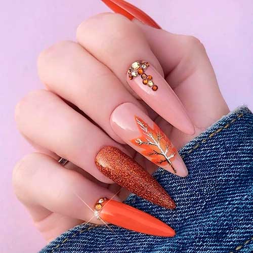 Classy almond orange nails with glitter, rhinestones, and autumn leaf on accent nail for autumn 2020