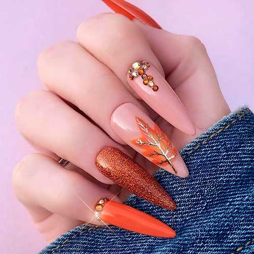 Classy almond orange nails with glitter, rhinestones, and autumn leaf on accent nail for autumn 2020