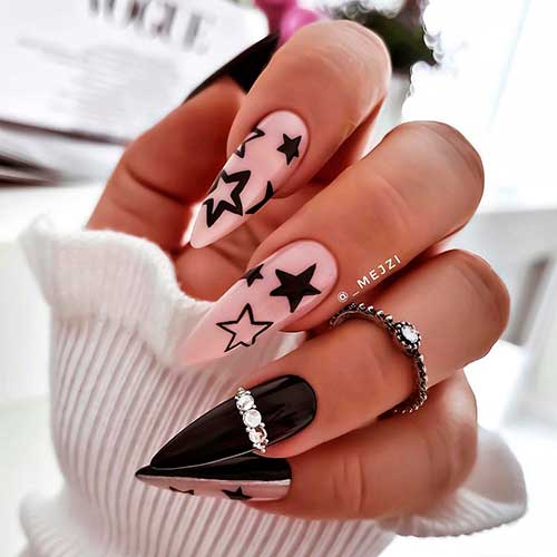 Almond shaped black nails with stars on two accent nude pink nails and rhinestones on ring fingernail design