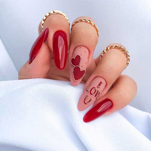 Dark red valentines day nails adorned with red heart shaped and some rhinestones over two nude colored accent nails