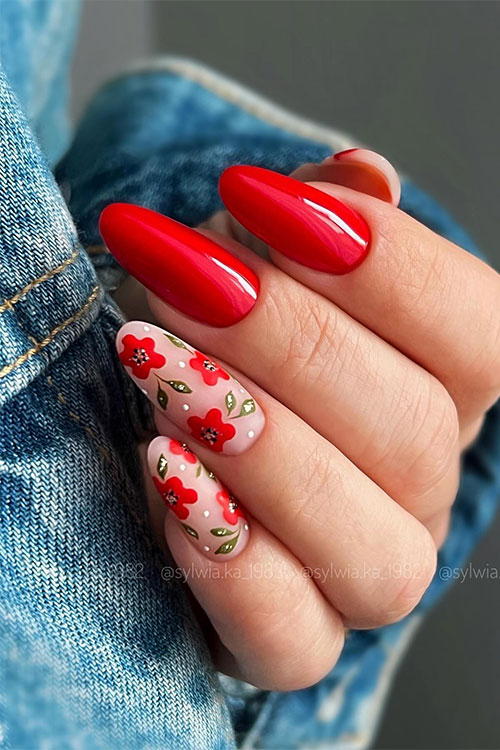 Long almond-shaped nude nails adorned with red flowers with olive green leaves, and two accent glossy red nails