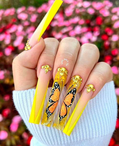 Long square bright yellow spring French tip nails with a butterfly on two accents and adorned with glitter and rhinestones
