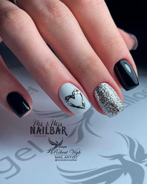 Short square shaped black nails with silver accent and another white accent adorned with silver glitter heart shape