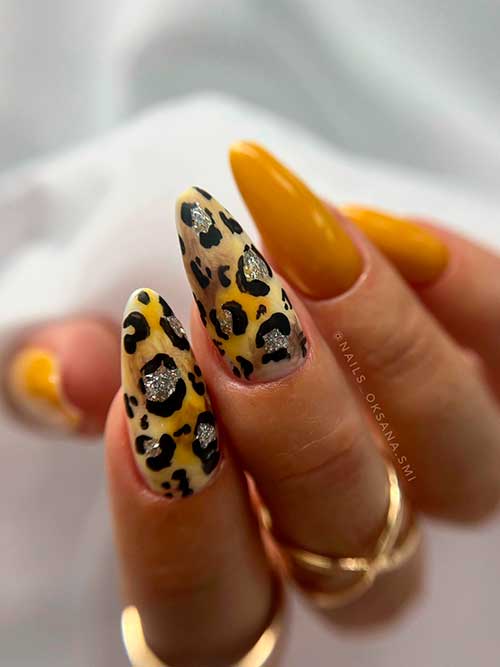 Long almond shaped mustard yellow fall nails with black leopard prints adorned with silver glitter