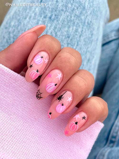 Pink pumpkin with black spider web nail art on a nude base color Long round shaped pink pumpkin with stars, and black spider web nail art on a nude base color