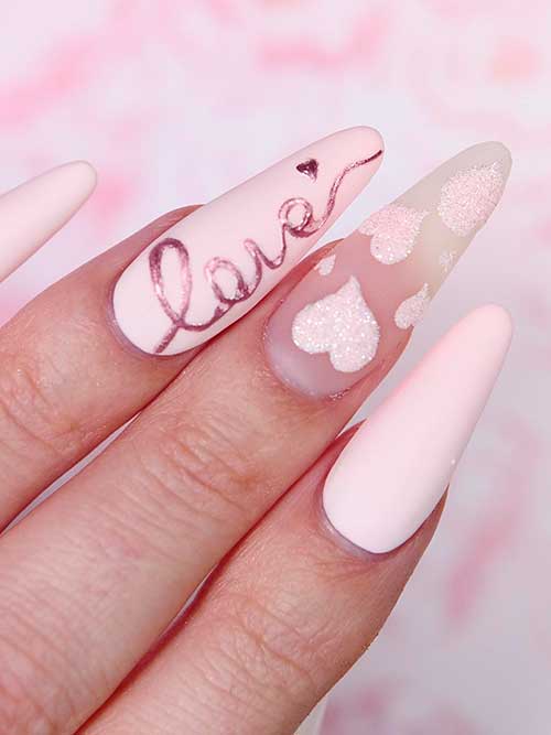 Long almond-shaped matte pastel pink valentine’s nails with love word and glitter hearts on accent nails
