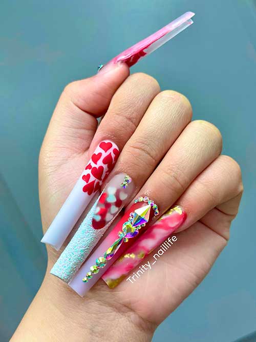 Long square shaped red and white valentine’s day nails adorned with small hearts, gold glitter, and rhinestones