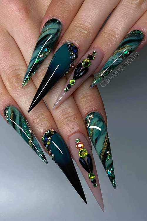 Long stiletto light to dark green marble fall nails with rhinestones, gold glitter, and a nude accent nail adorned with gems