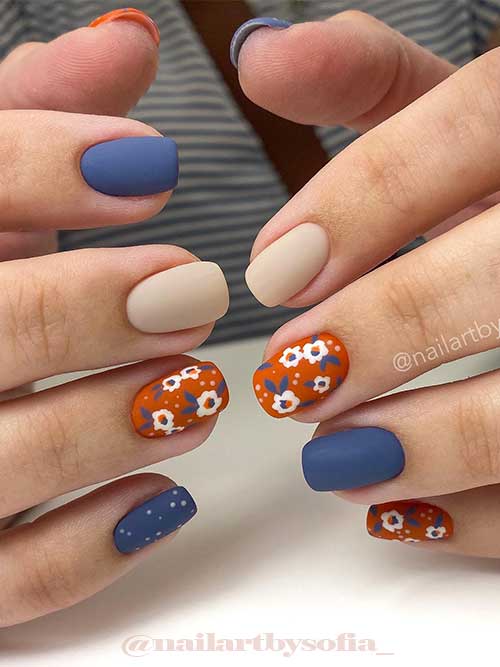 Short matte fall nails features burnt orange with flowers, denim blue, and beige colors