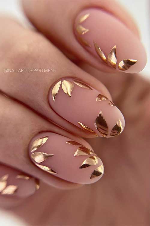 Short round matte nude base color nails with gold chrome fall leaves Short round matte nude base color nails with gold chrome fall leaves