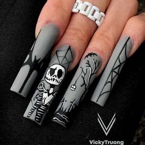 Long matte grey nails with black and white Halloween nail art ideas feature a skeleton, cemetery, cobweb, and bat