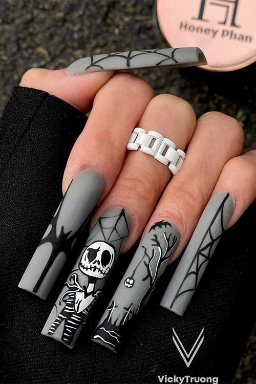 Long matte grey nails with black and white Halloween nail art ideas feature a skeleton, cemetery, cobweb, and bat Long matte grey nails with black and white Halloween nail art ideas feature a skeleton, cemetery, cobweb, and bat