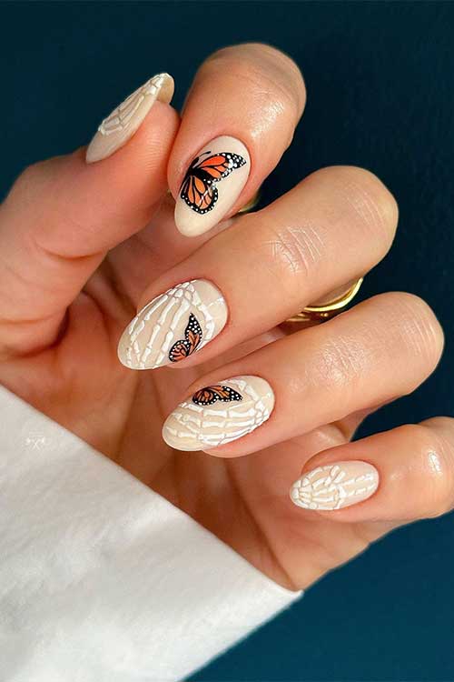Short beige nails with an off-white skeleton hand on each nail and adorned with black-orange butterflies