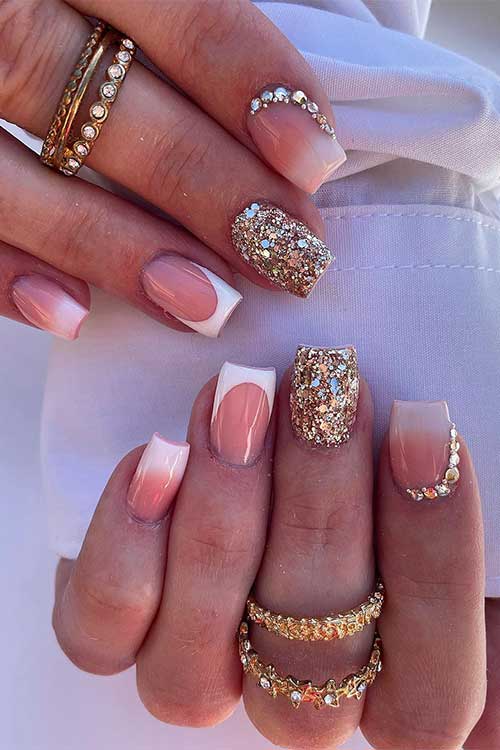 Short classy French tip nails with rhinestones and gold glitter on accent nails.