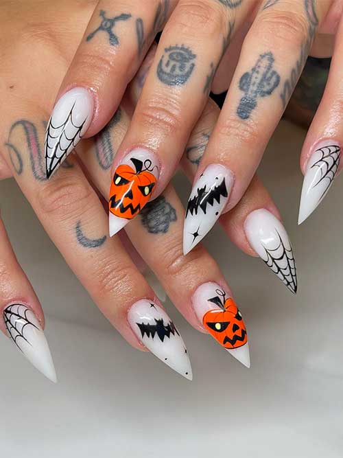Stiletto milky white Halloween nails feature black cobwebs and bats and an orange spooky pumpkin on an accent nail