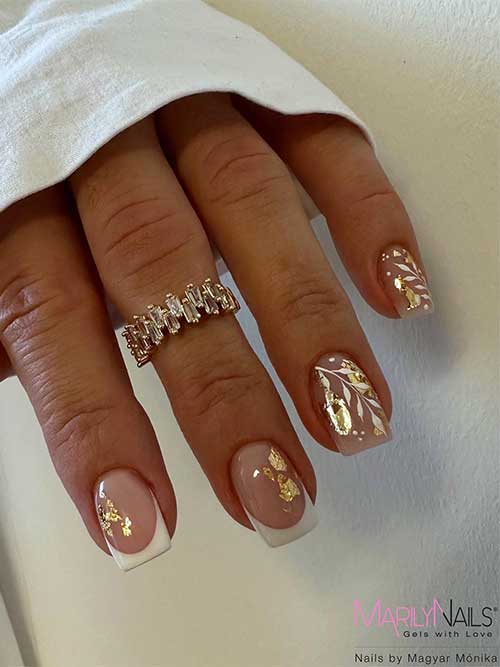 White French tip nails with gold foil flakes and white leaves on two nude accent nails.
