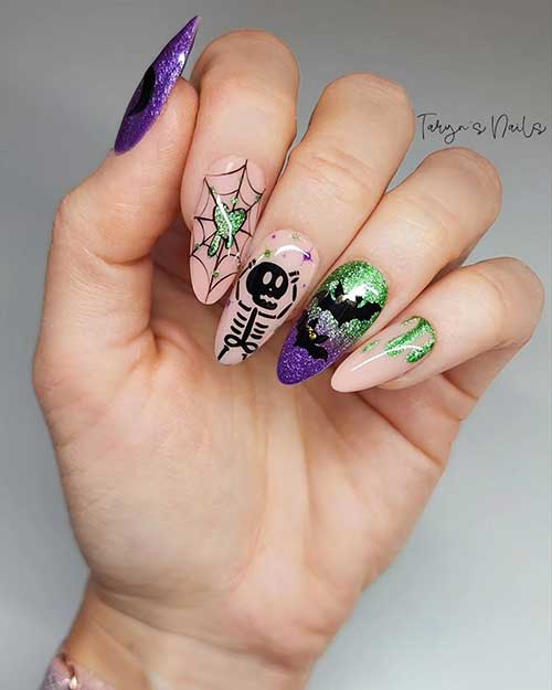 A cute nude Halloween manicure features a cobweb, a skeleton, and bats that are adorned with glitter purple and green colors