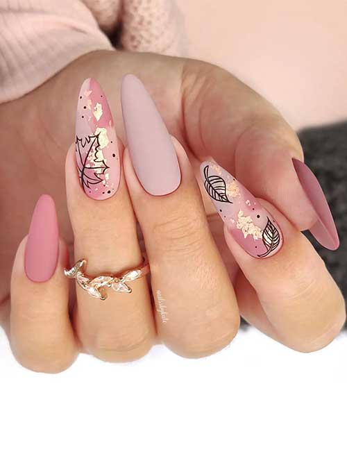 Nude pink fall season nails with fresh and light nude pink hues adorned with black leaves and gold flakes on two accents