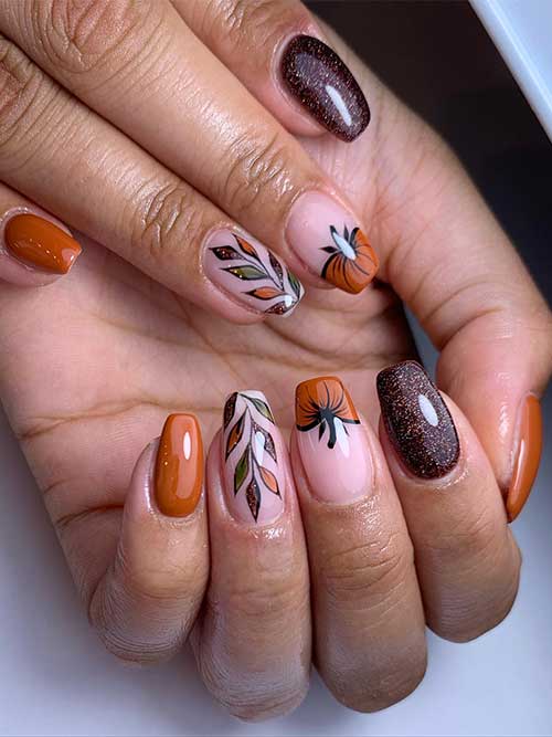 Short burnt orange coffin nails with a pumpkin French tip nail, a glitter brown accent nail, and a leaf nail art accent