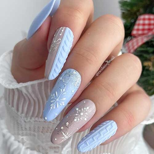Ice-blue winter nails feature sweater nail art, snowflakes, silver glitter, and a beige accent nail with snowflakes