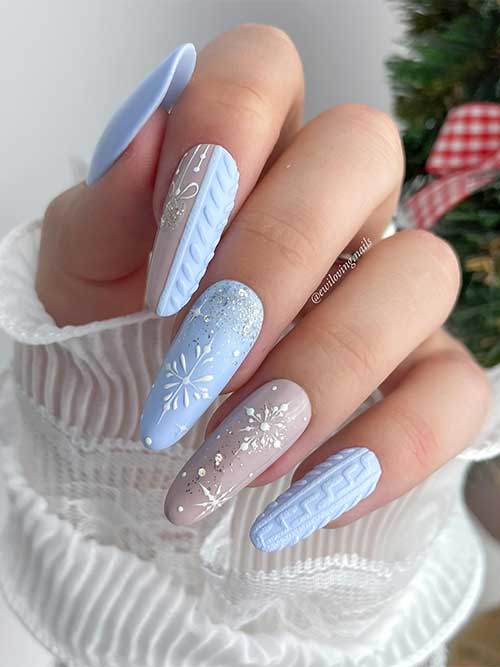 Ice-blue winter nails feature sweater nail art, snowflakes, silver glitter, and a beige accent nail with snowflakes
