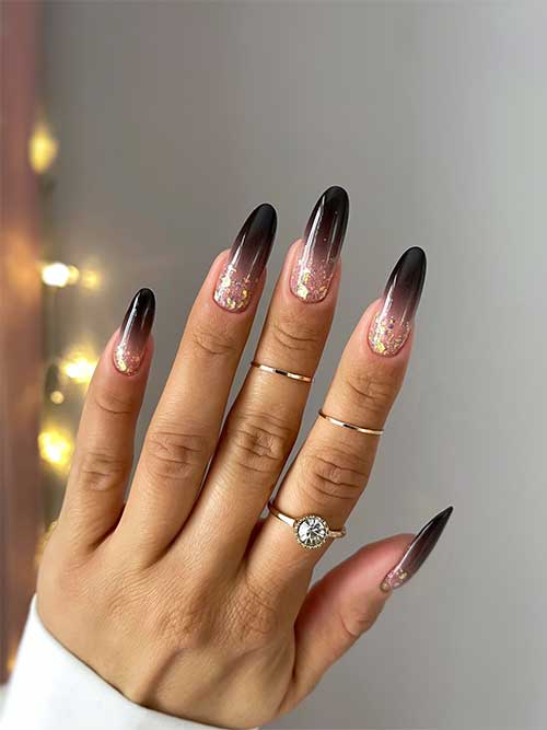 Long glossy black ombre nails with gold glitter above the cuticles