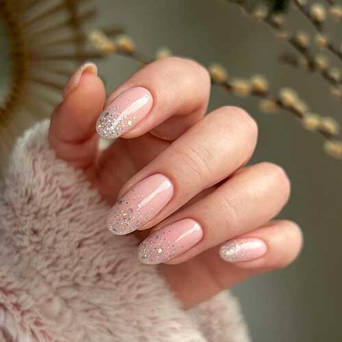 Nude pink New Year’s nails with gold and mixed colors glitter on the nail tips