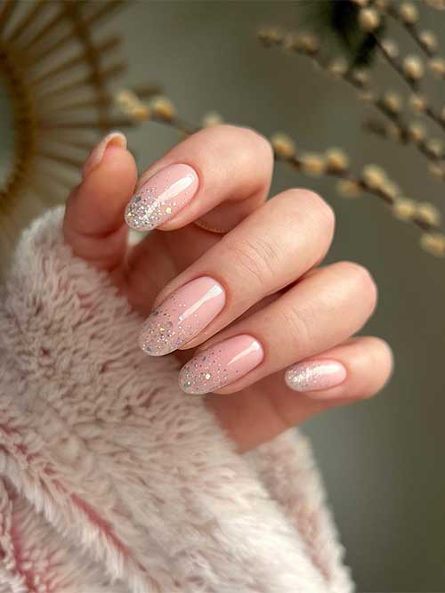Nude pink New Year’s nails with gold and mixed colors glitter on the nail tips