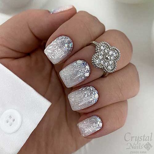 Short silver glitter nails with white snowflakes and holographic flakes are one of the best New Year's nail designs