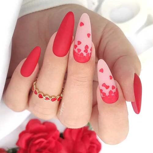 Gorgeous matte red Valentine’s nails with two accent nude pink nails adorned with red fallen heart nail art.
