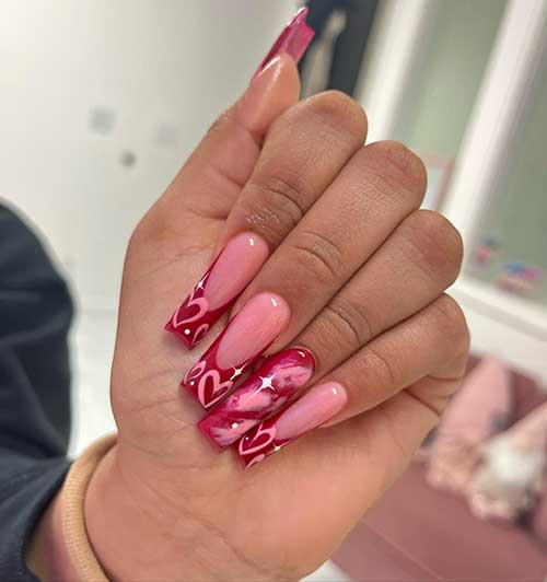 Long red French tip nails with pink hearts and tiny stars on the tips. Besides, an accent red nail with a pink marble effect