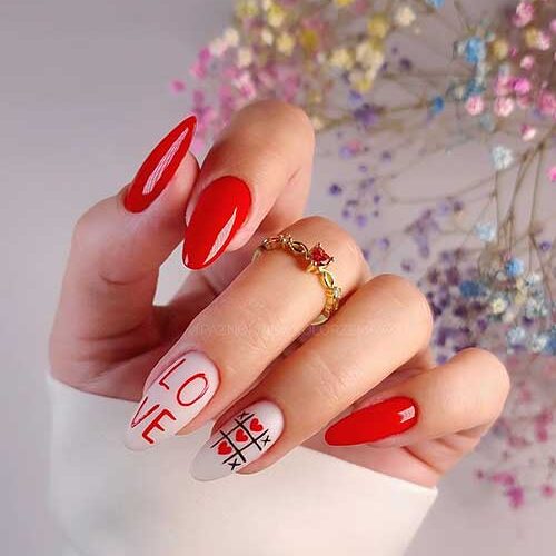 Red and white Valentine’s nail design with glossy red nails and two accent white nails with “LOVE” letters and XO nail art