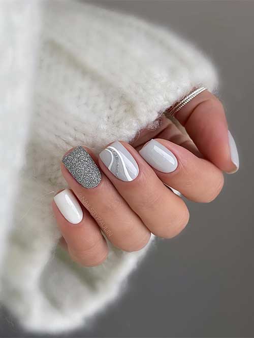 Short light grey nails with silver glitter on an accent nail, a white accent nail, and a grey nail adorned with swirls