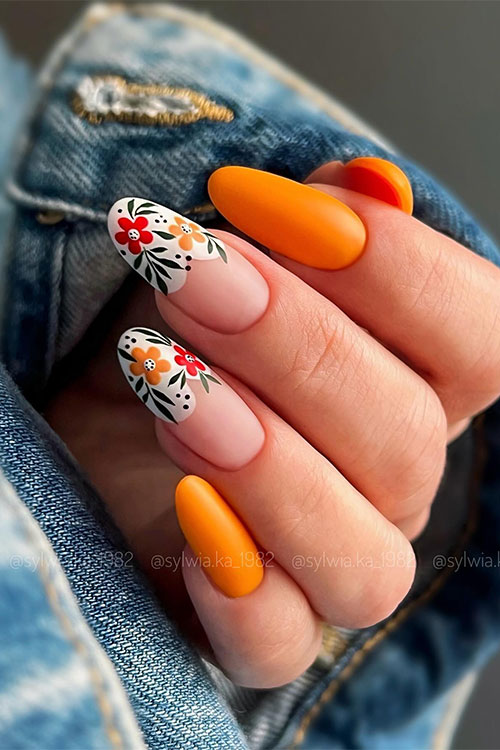 Bold matte orange spring nails with two accent nude nails adorned with flowers are perfect spring nail ideas with flowers