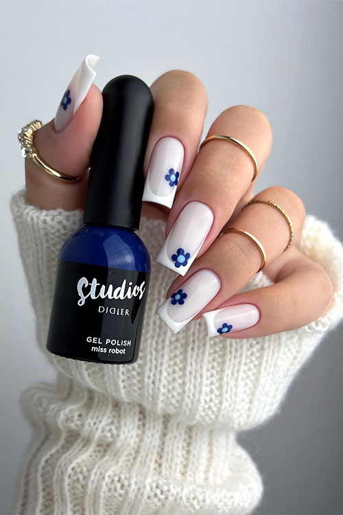 Long square-shaped white French tip nails over milky white base color and adorned with navy flowers