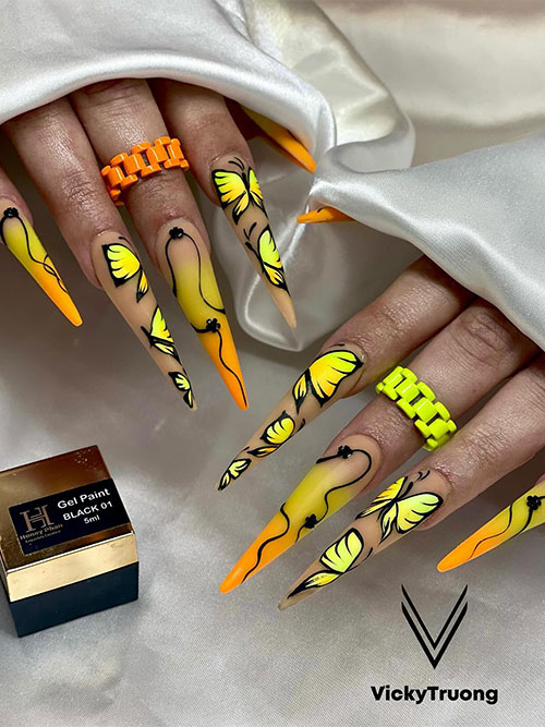 Long nude nails with three neon yellow and orange ombre nails and two accents with neon yellow and orange butterflies