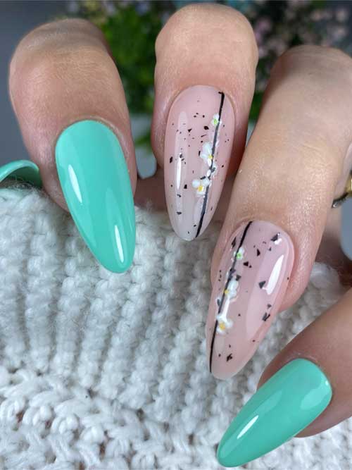 Fresh green spring nail design with mint and nude tones, featuring white floral patterns and black speckles on almond-shaped nails. Fresh green spring nail design with mint and nude tones, featuring white floral patterns and black speckles on almond-shaped nails.