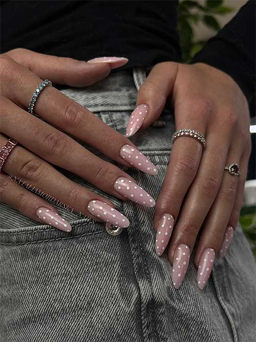 Pastel pink polka dot summer nails with white dots on an almond shape, paired with delicate rings in blue, pink, and silver. Pastel pink polka dot summer nails with white dots on an almond shape, paired with delicate rings in blue, pink, and silver.